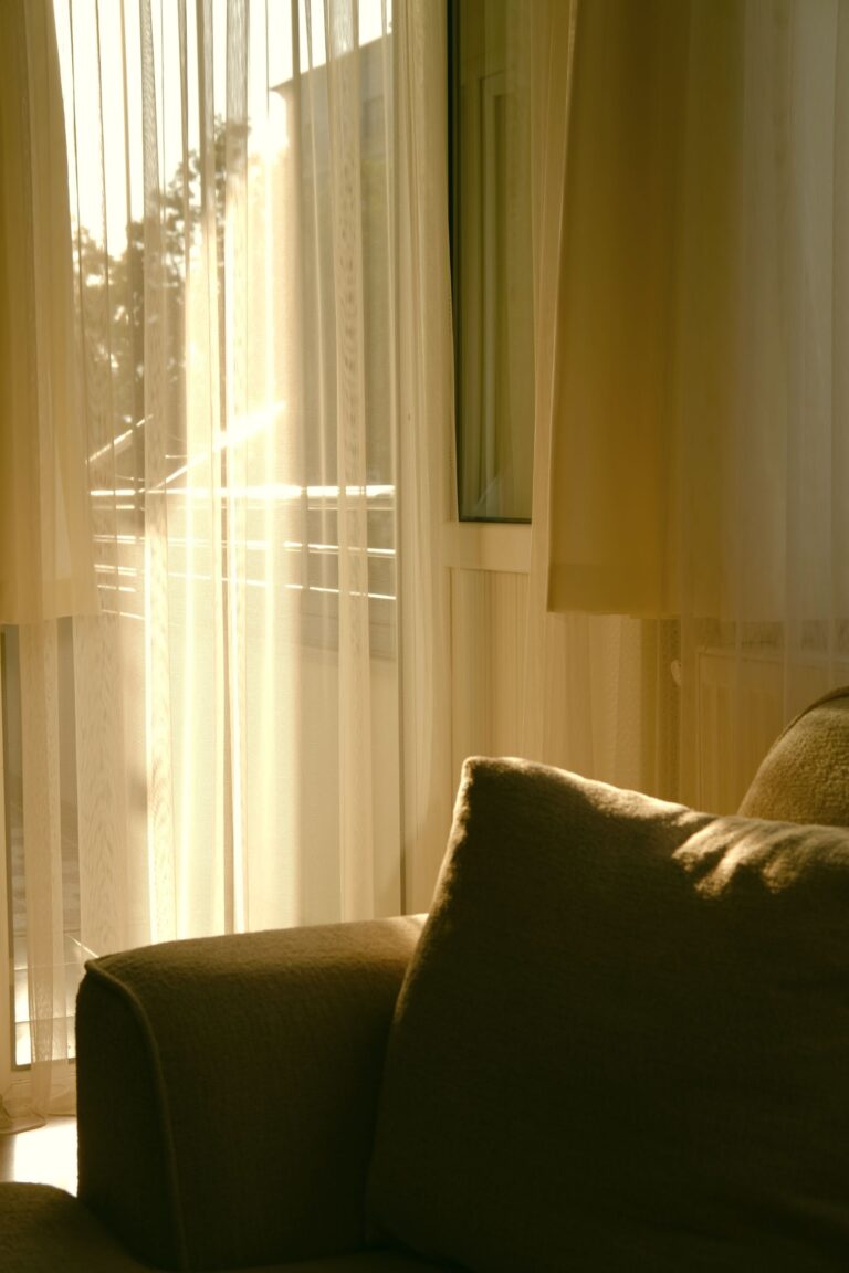 Warm evening sunlight through sheer curtains onto a cozy sofa